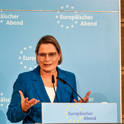 Eine Frau steht hinter einem Rednerpult und spricht in ein Mikrofon