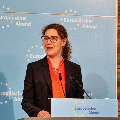 Eine Frau und ein Mann stehen mit Ordnern in der Hand in einem Foyer und diskutieren