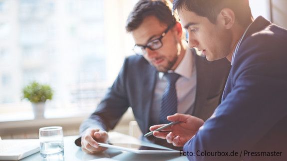 Zwei Männer im Büro sehen gemeinsam auf Tablet und besprechen sich