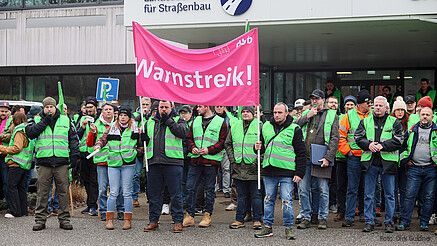 Das Foto zeigt demonstrierende Straßenwärter. Sie tragen grüne Streikwesten.