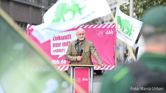 Ein Mann steht im Mittelpunkt des Bildes und spricht in ein Mikrofon