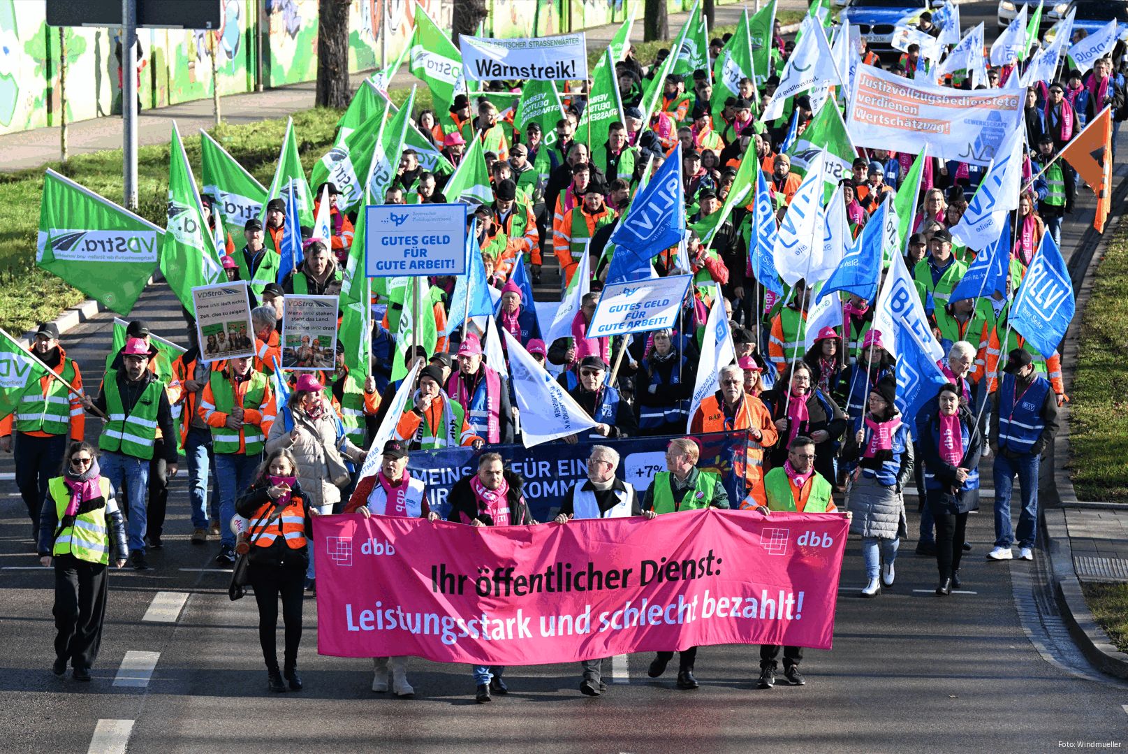 Luftaufnahme von einer Gruppe Menschen, die mit bunten Fahnen und Warnwesten auf einer Straße demonstrieren