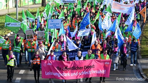 Luftaufnahme von einer Gruppe Menschen, die mit bunten Fahnen und Warnwesten auf einer Straße demonstrieren