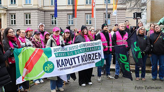 Eine Gruppe Menschen demonstriert mit Bunten Bannern und Warnwesten auf einem Platz.